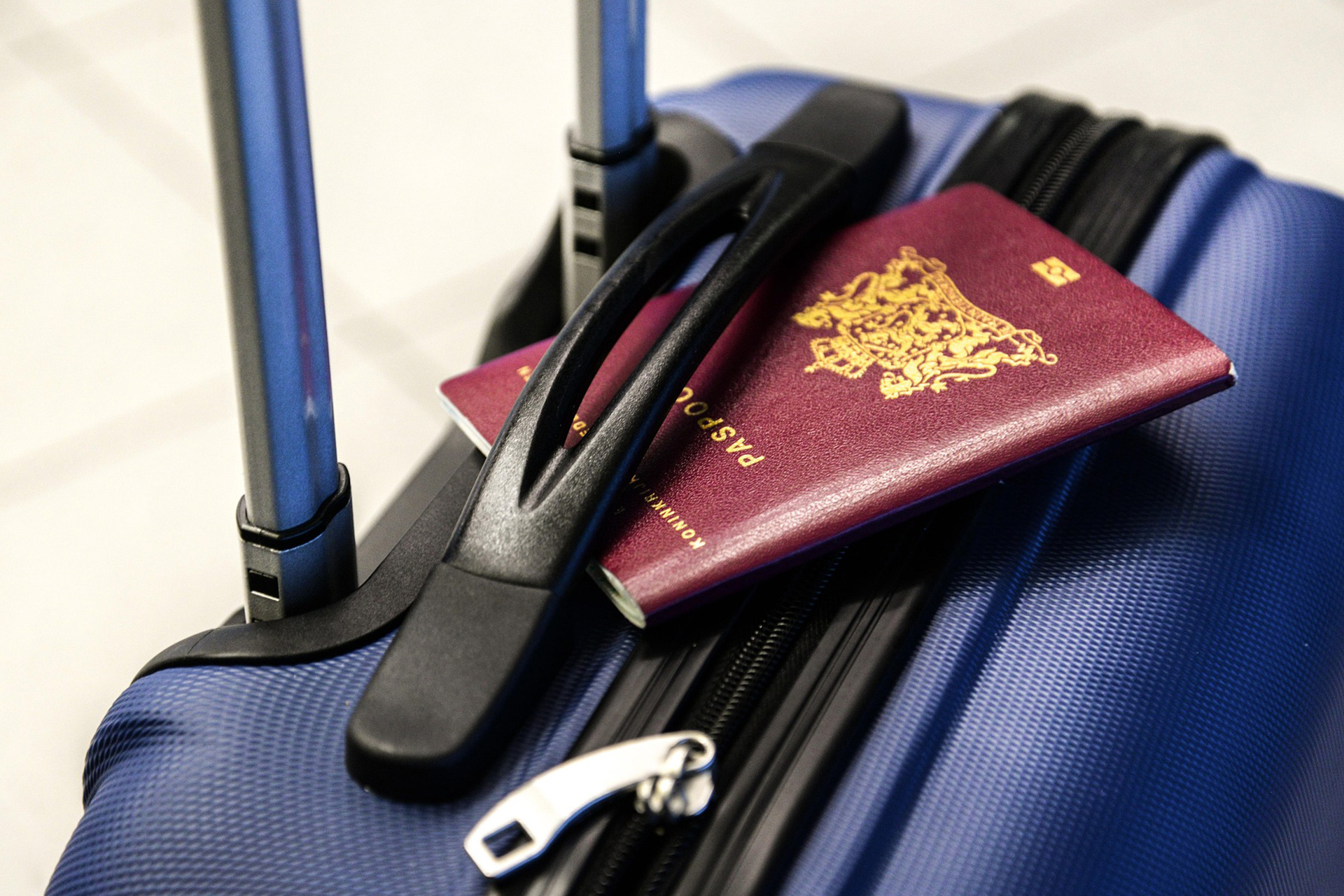 Bordeauxroter Reisepass liegt auf einem blauen Rollkoffer mit ausgezogenem Griff, bereit für die Reise – Symbol für Urlaub und Aufbruch.